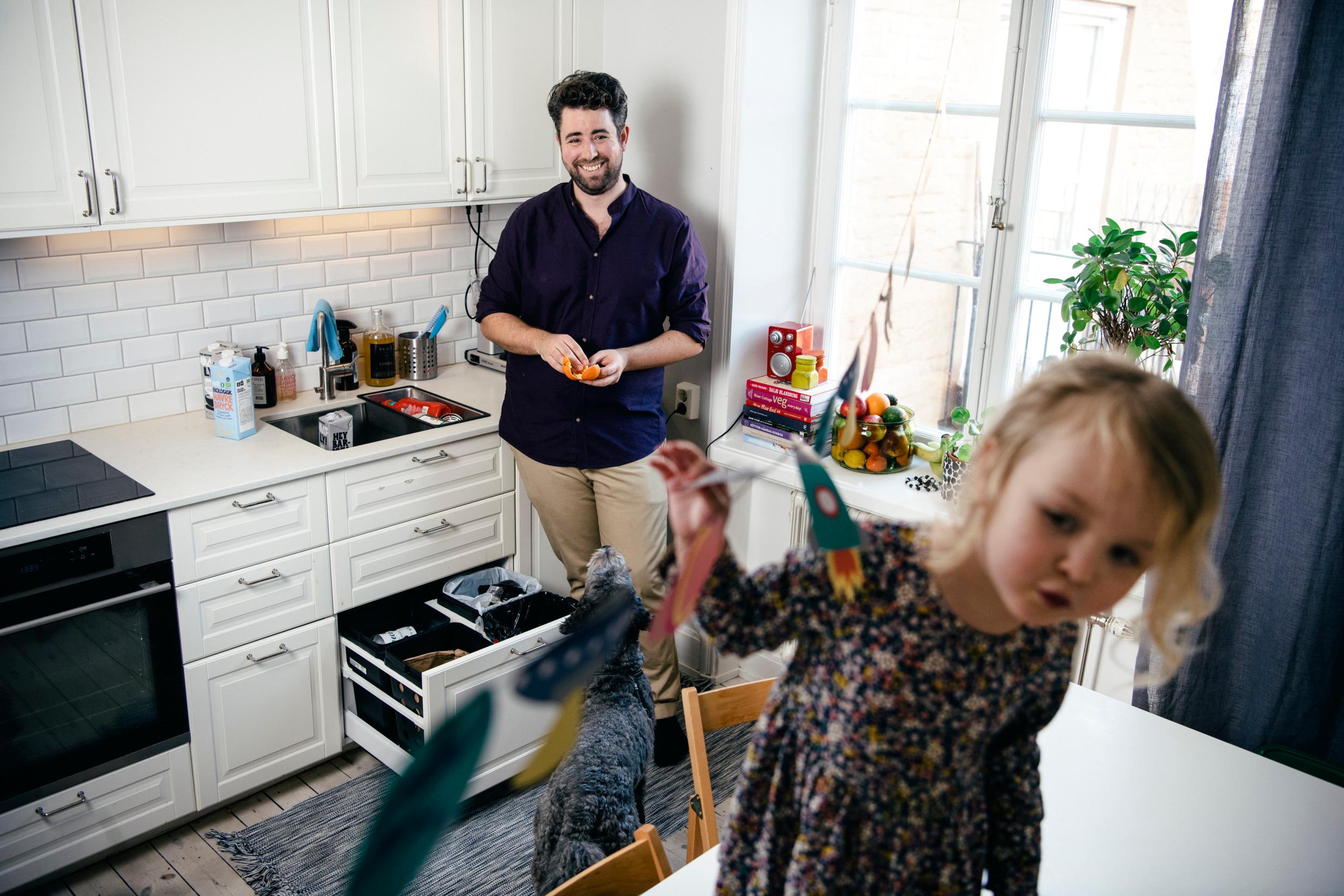 A father and his daughter in a kitchen by a drawer with recycling.