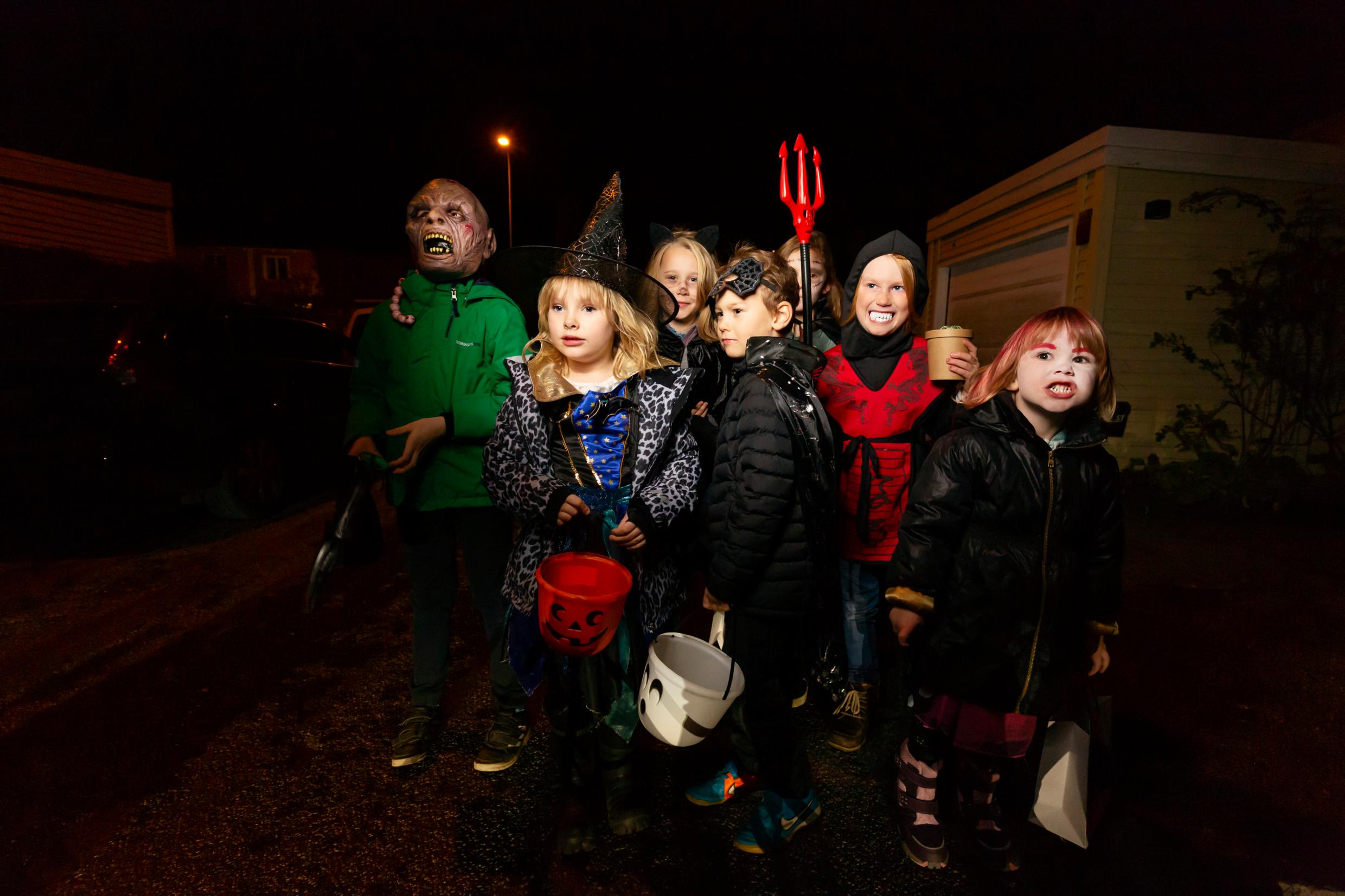 A group of children in costumes walking down a dark street.