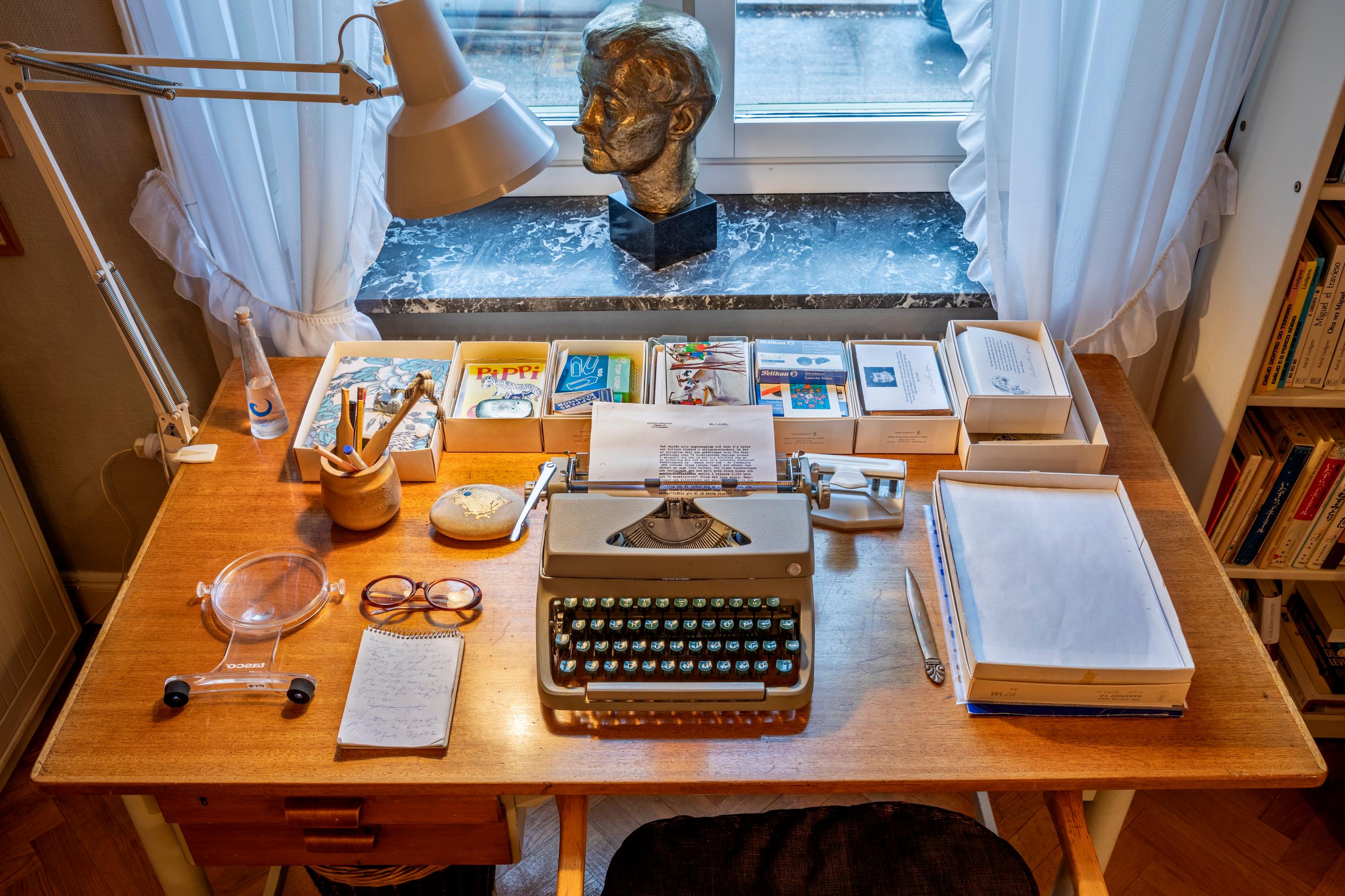A desk with a reading lamp, a typewriter, books and other artifacts.