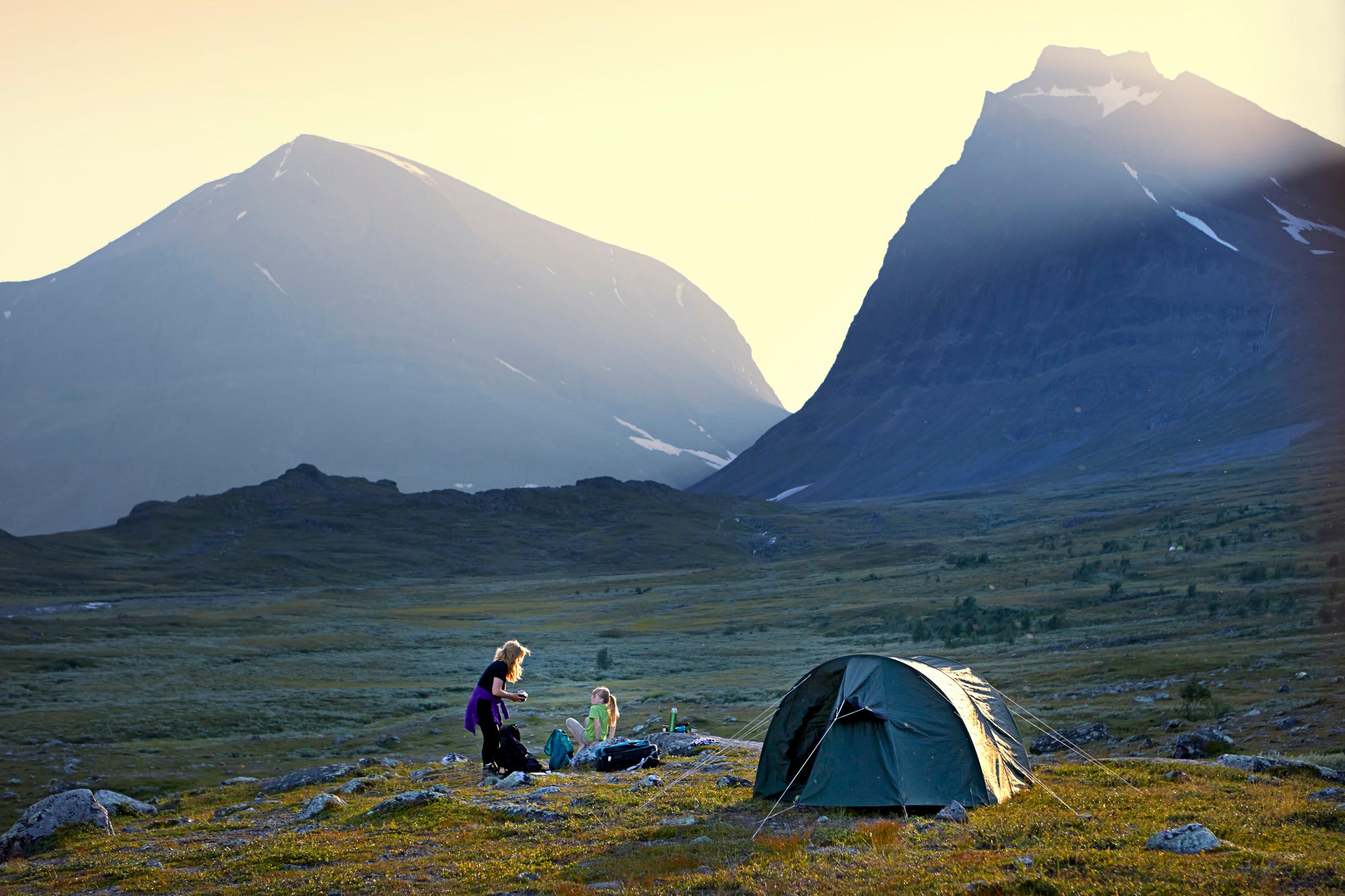 Two people next to a tent, with tall mountains in the background.