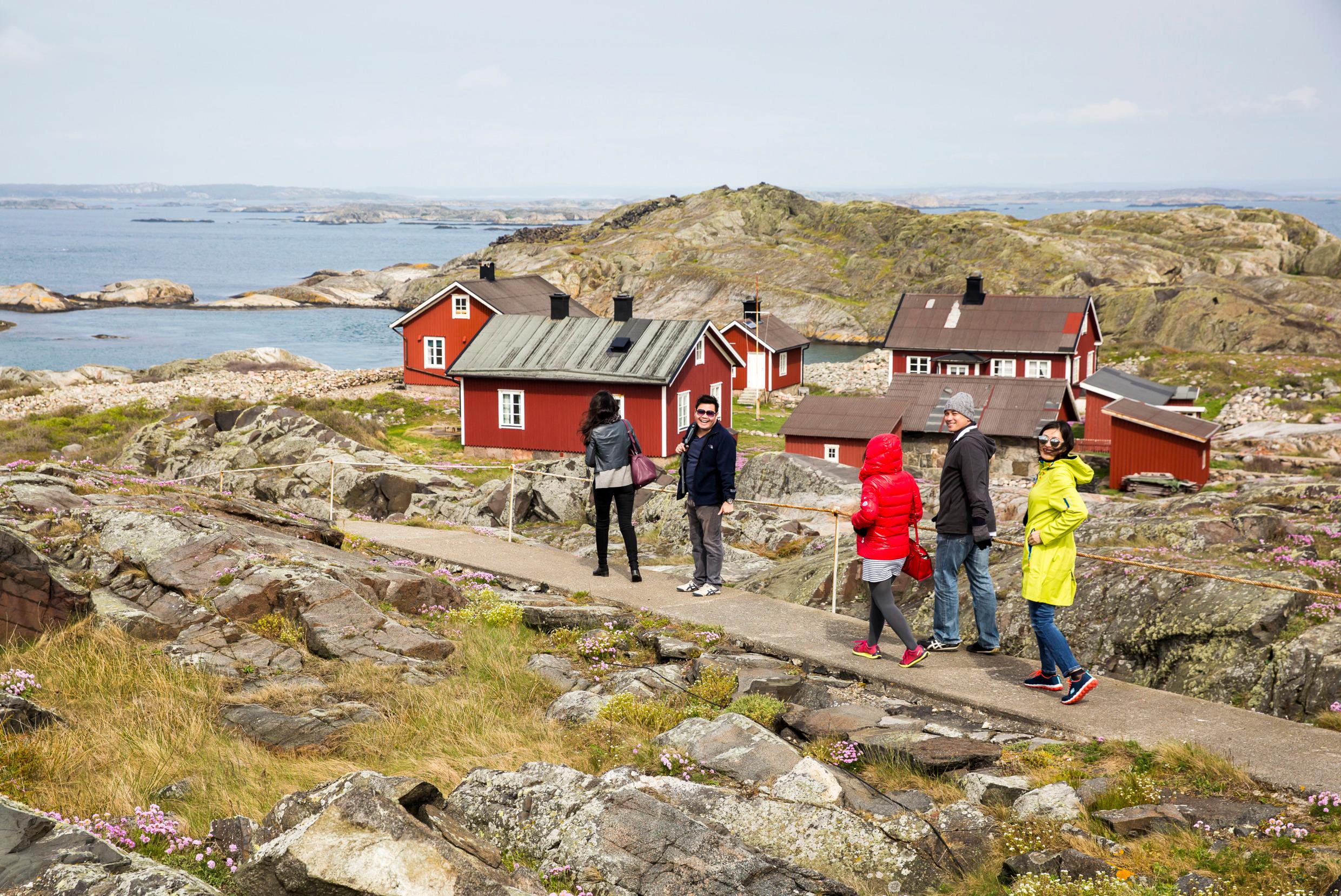 A group of people walk through the rocky island landscape of Kosterhavet National Park, passing a few small red houses. Summer in Sweden can look very different, depending on where you go.