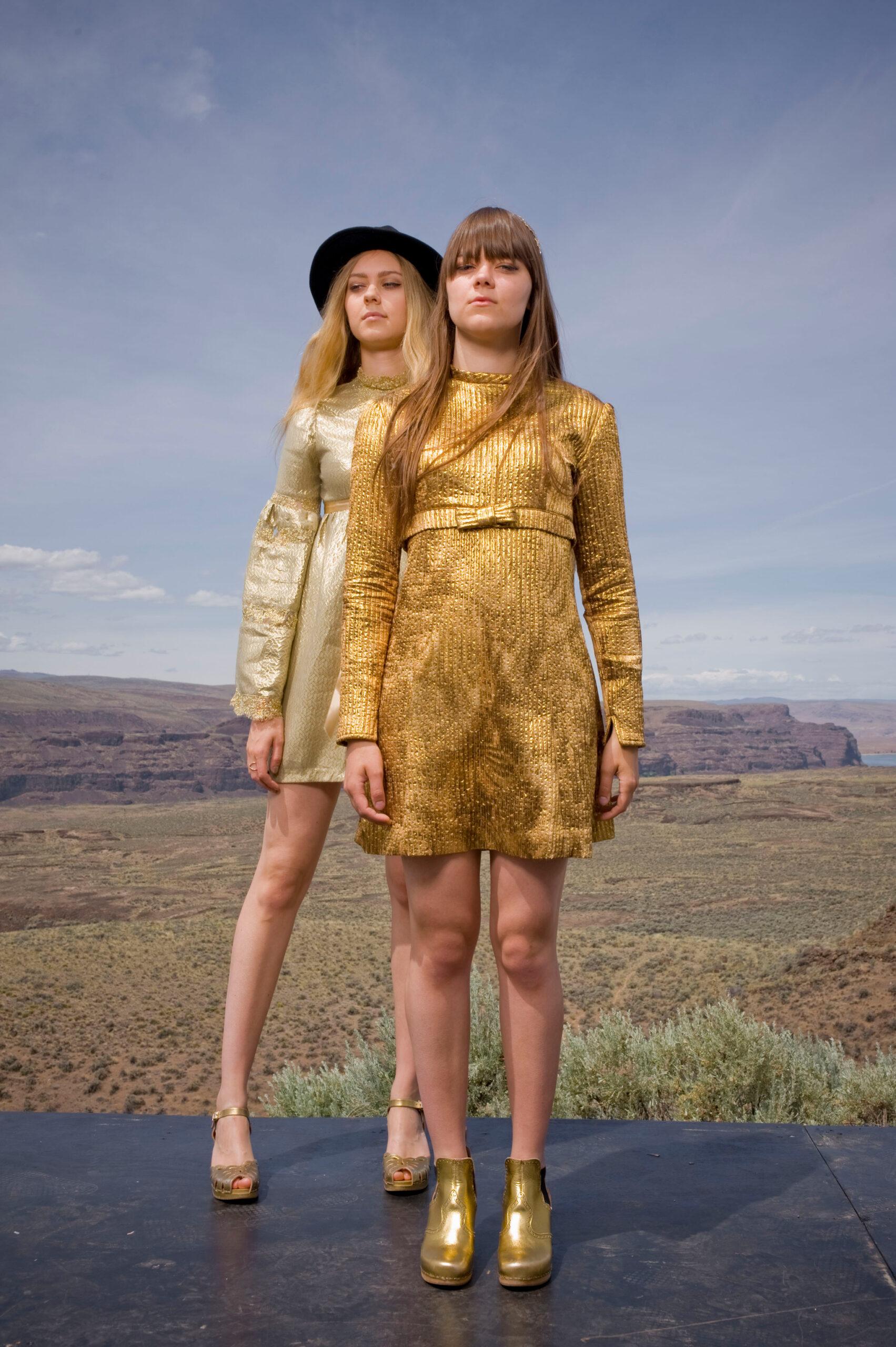 The two sisters of First Aid Kit posing against a backdrop showing a vast landscape.