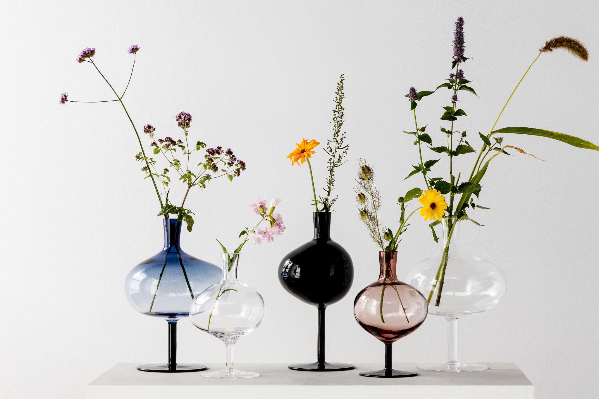 Five glass vases on a foot. All vases have fresh flowers in them.