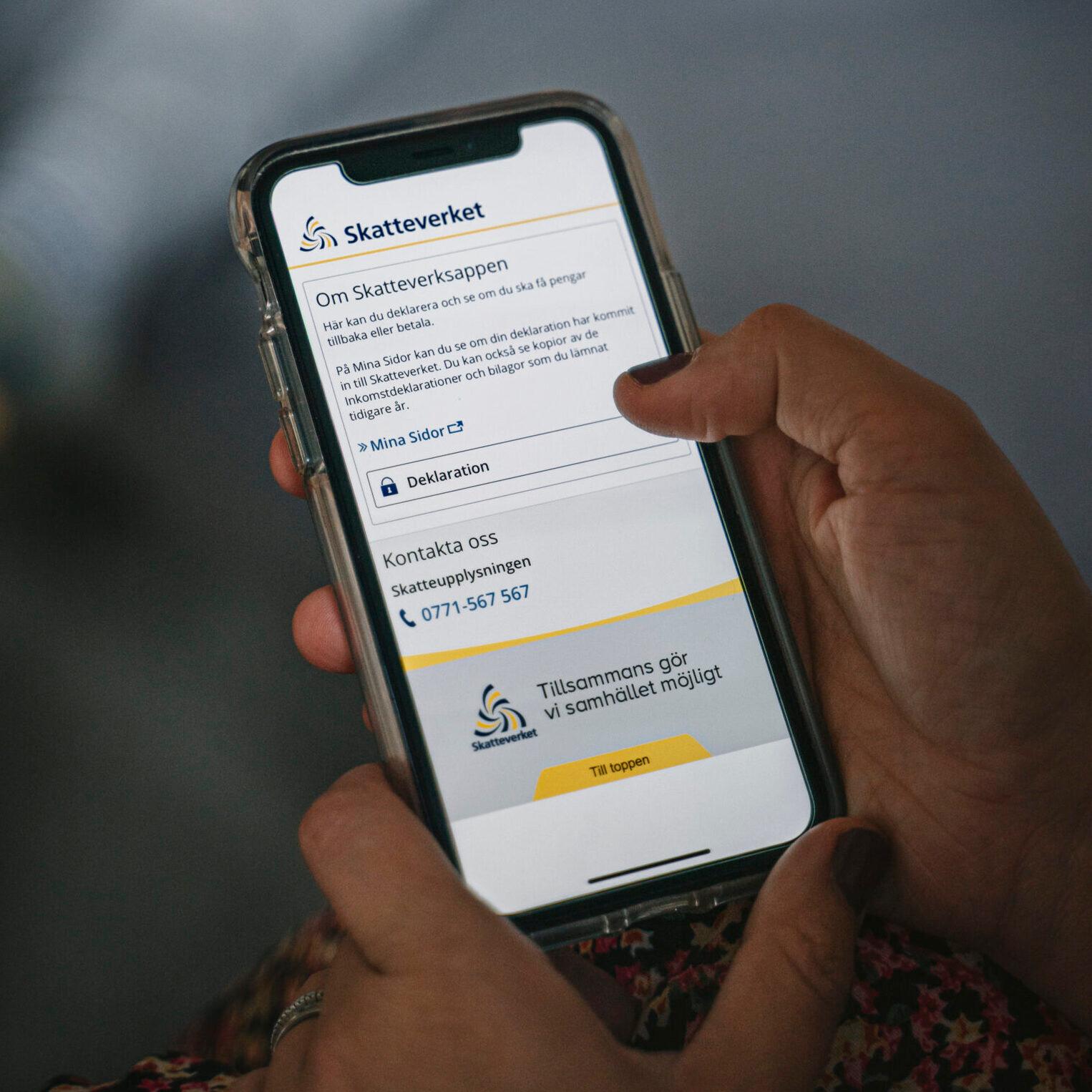 A hand holding a mobile phone with the Swedish Tax Agency app on the screen. Knowing the tax system helps when starting a business in Sweden.