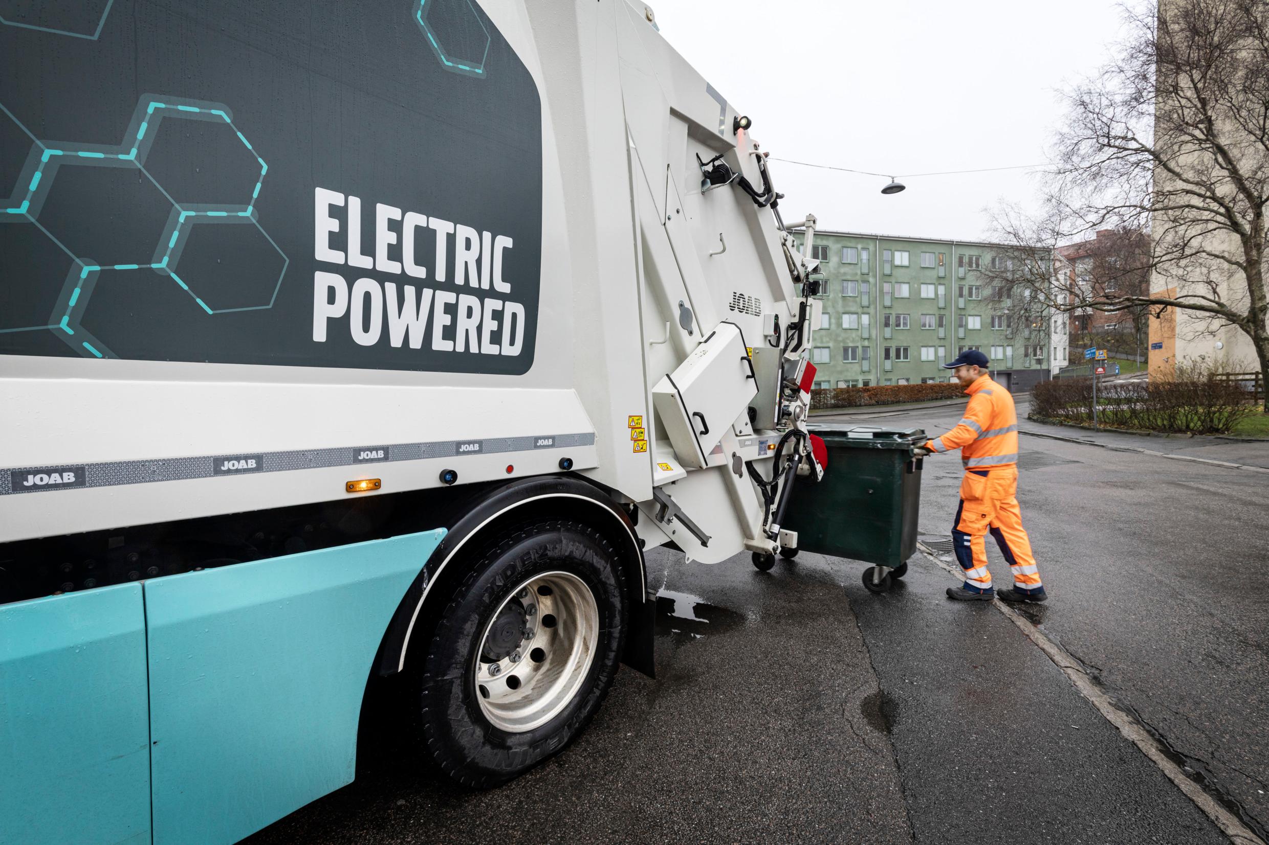 A man is pushing a waste bin toward a truck.