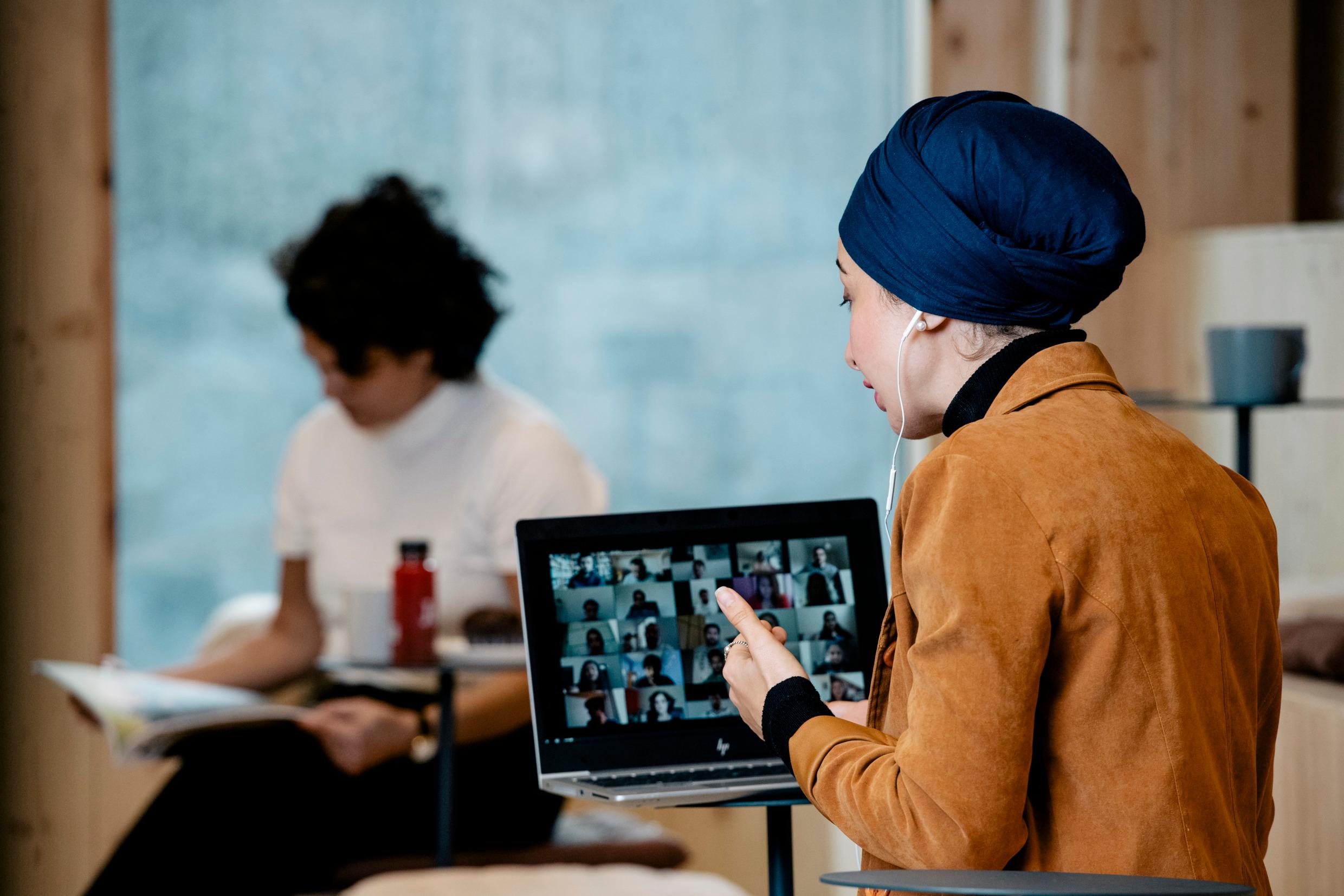 A woman sits in front of a small desk that holds a laptop. She as an ear-piece and is gesturing with her hand.