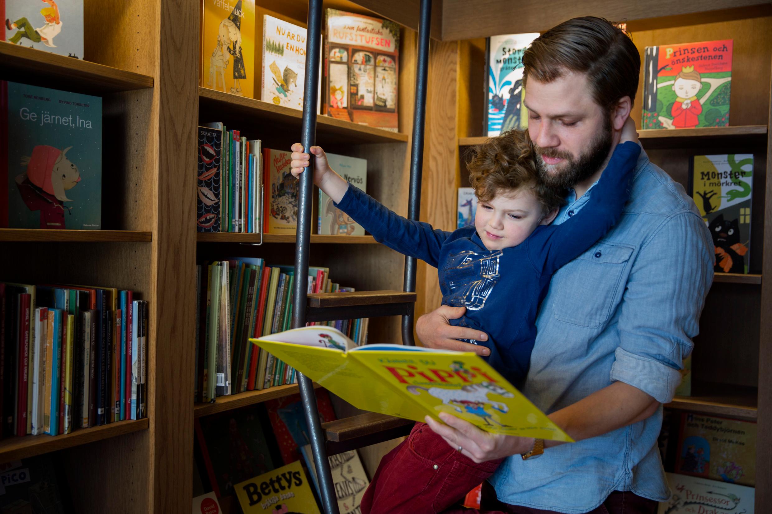 A son leaning against his father, who holds an open book in his hand.