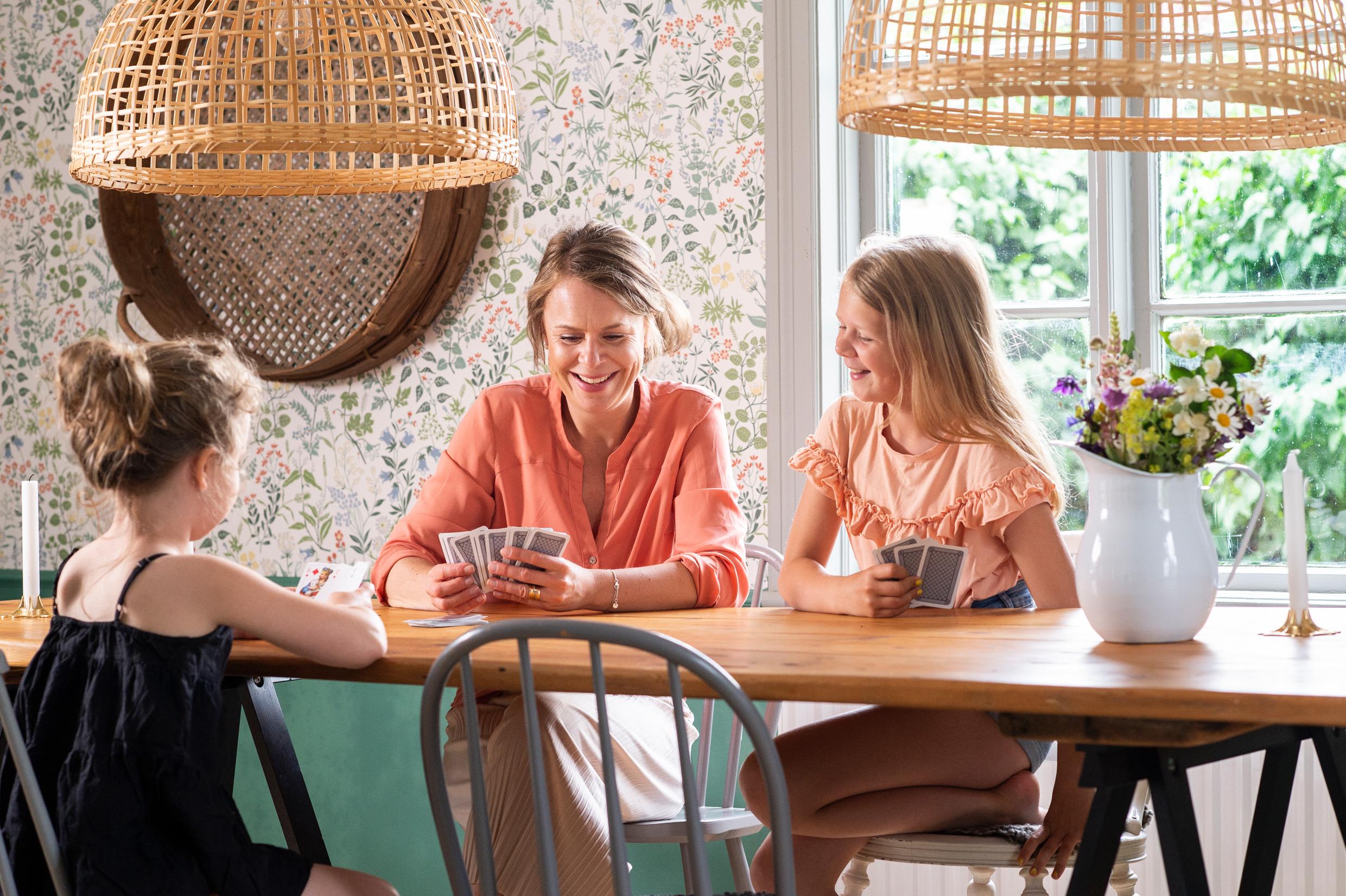 A woman and two girls sitting around a table playing cards. There a vase with flowers on the table.