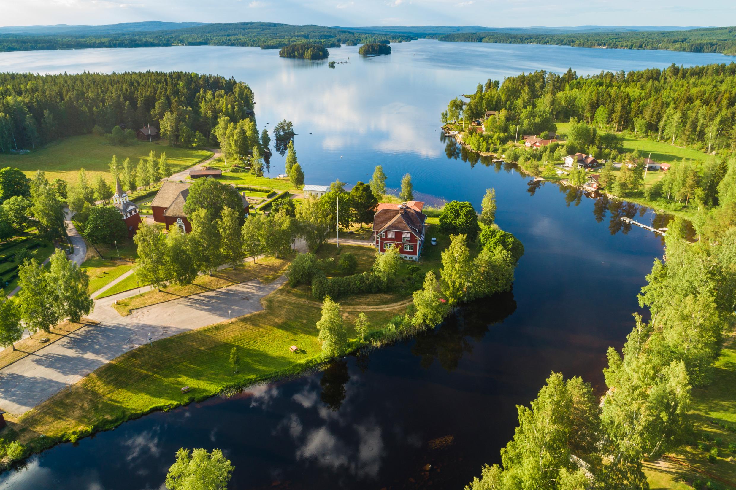 An aerial view of a river that leads to Toftan Lake. There is a red house near the water surrounded by greenery.