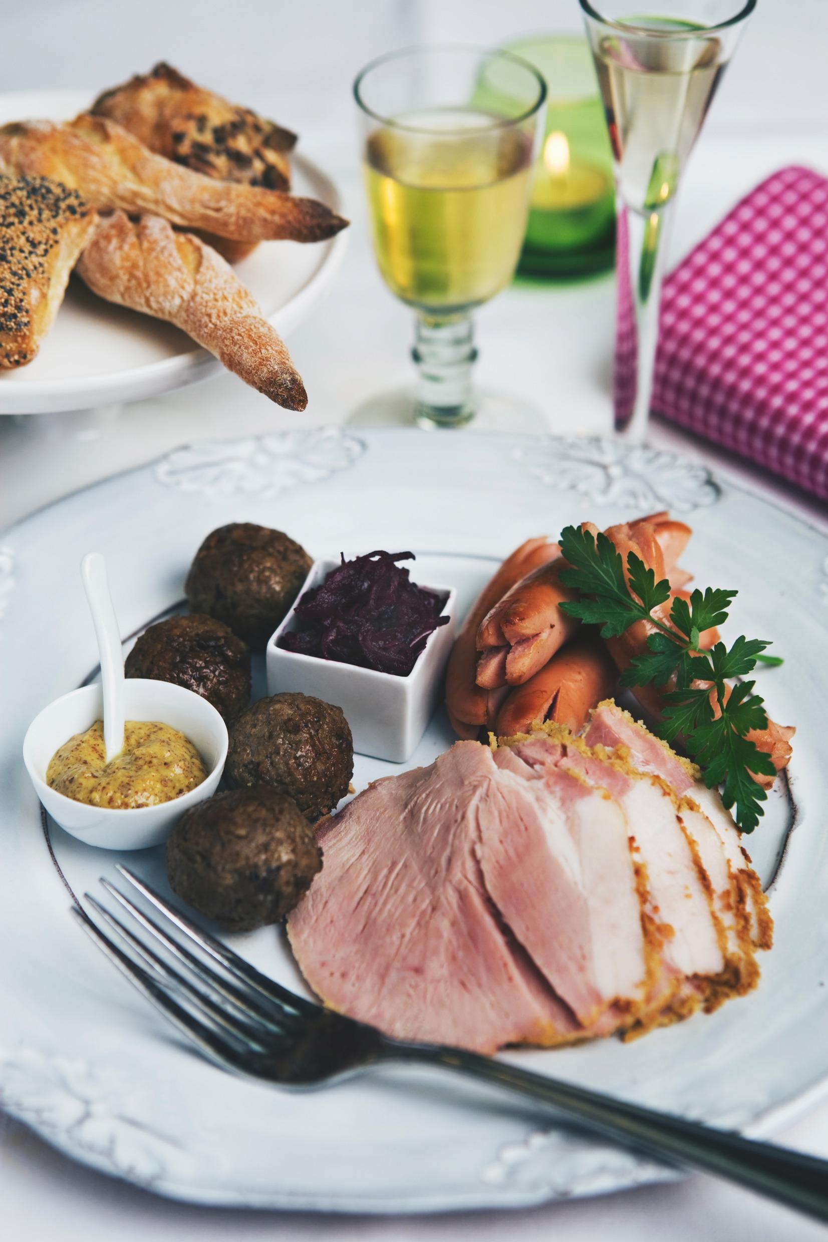 A plate with Christmas food such as ham and meatballs.