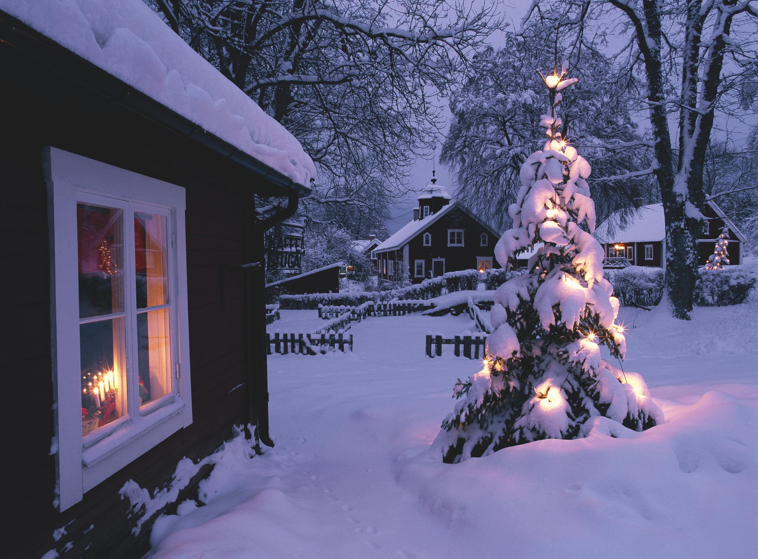 Snow profusely cover red and white houses and an outdoor decorated tree.