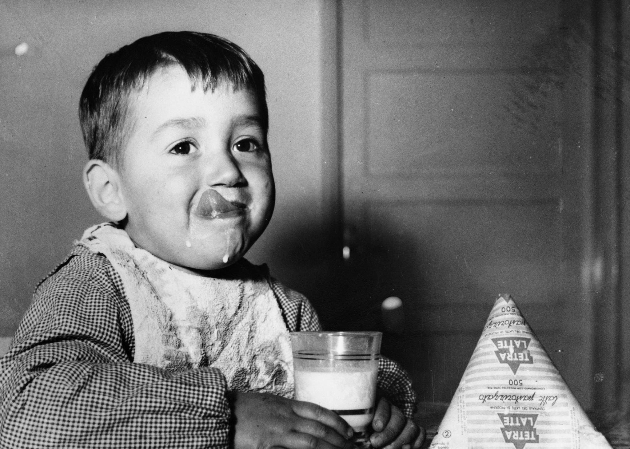 A young boy with hit tongue out, milk running down his chin.