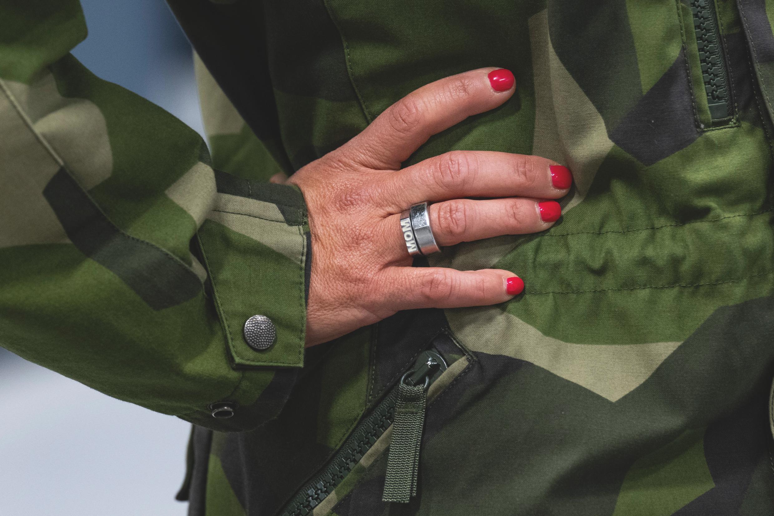 Close-up of a woman's arm and torso, in fatigue, revealing painted finger nails and a wedding band with the text 'mom'.