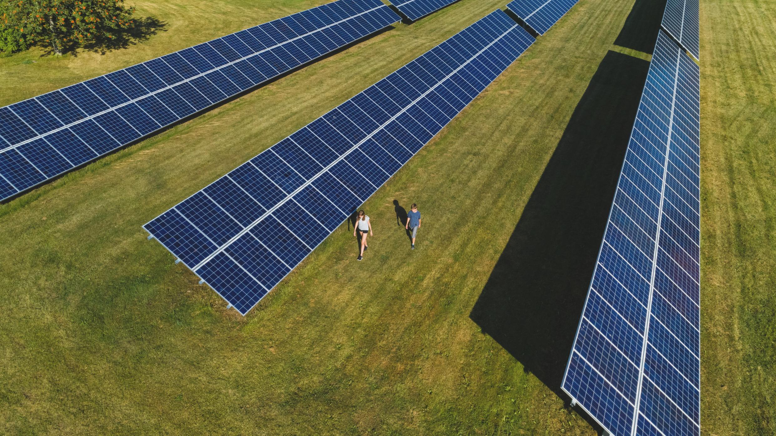 Two children walk by large solar panels.